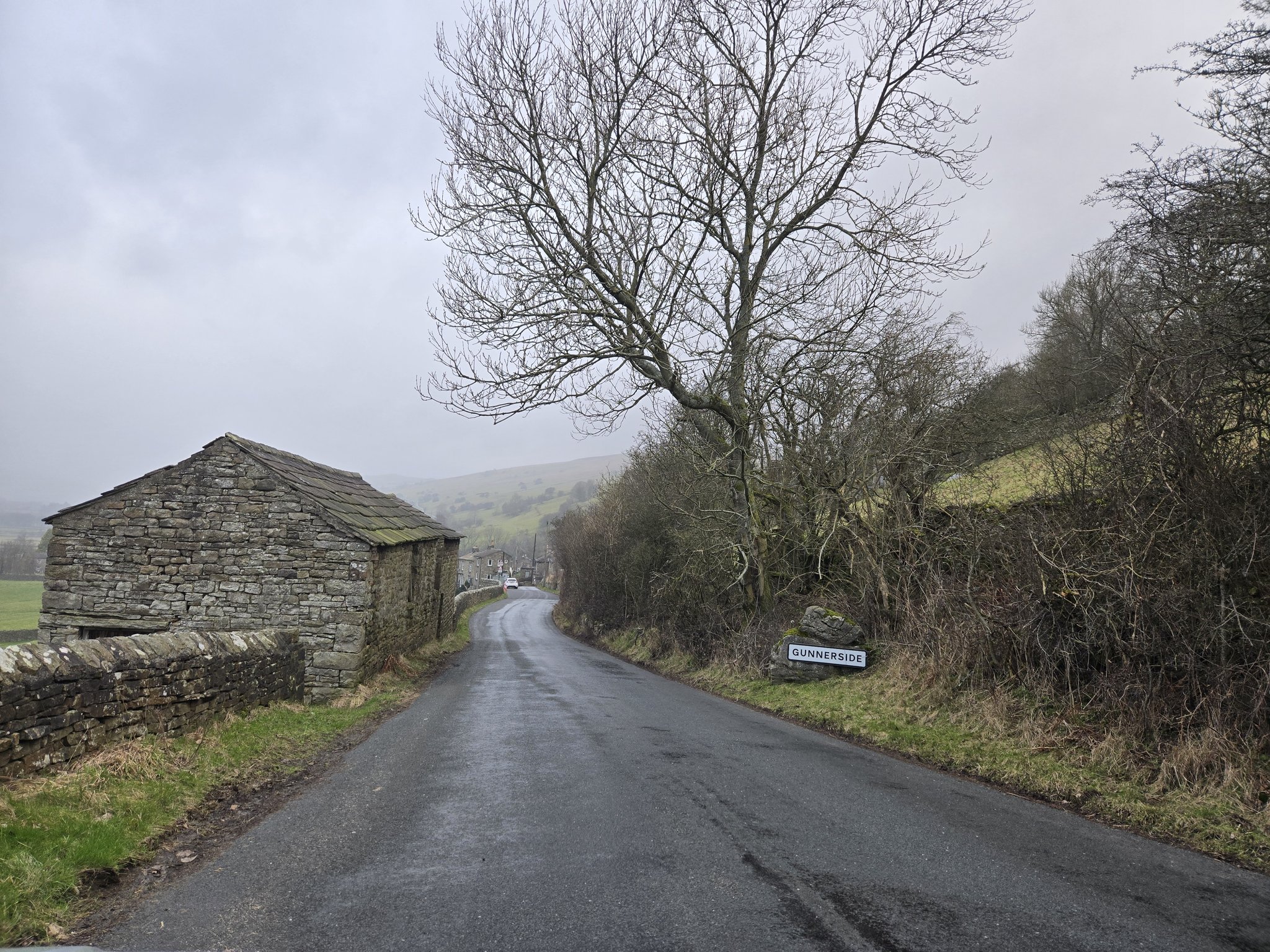 road leading in to village with barn on one side and bare tree on the other