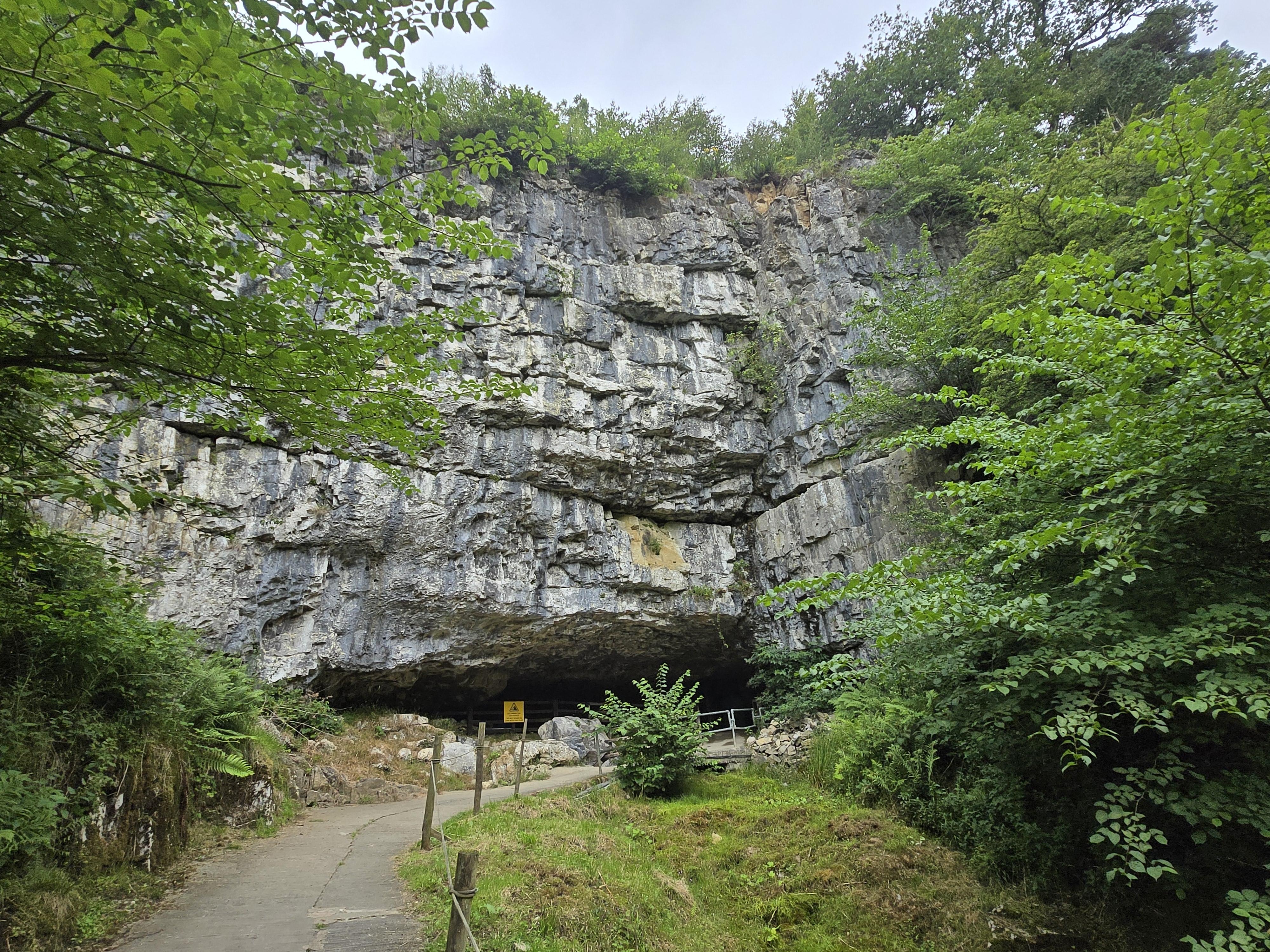 Wide cave entrance at base of limestone cliff